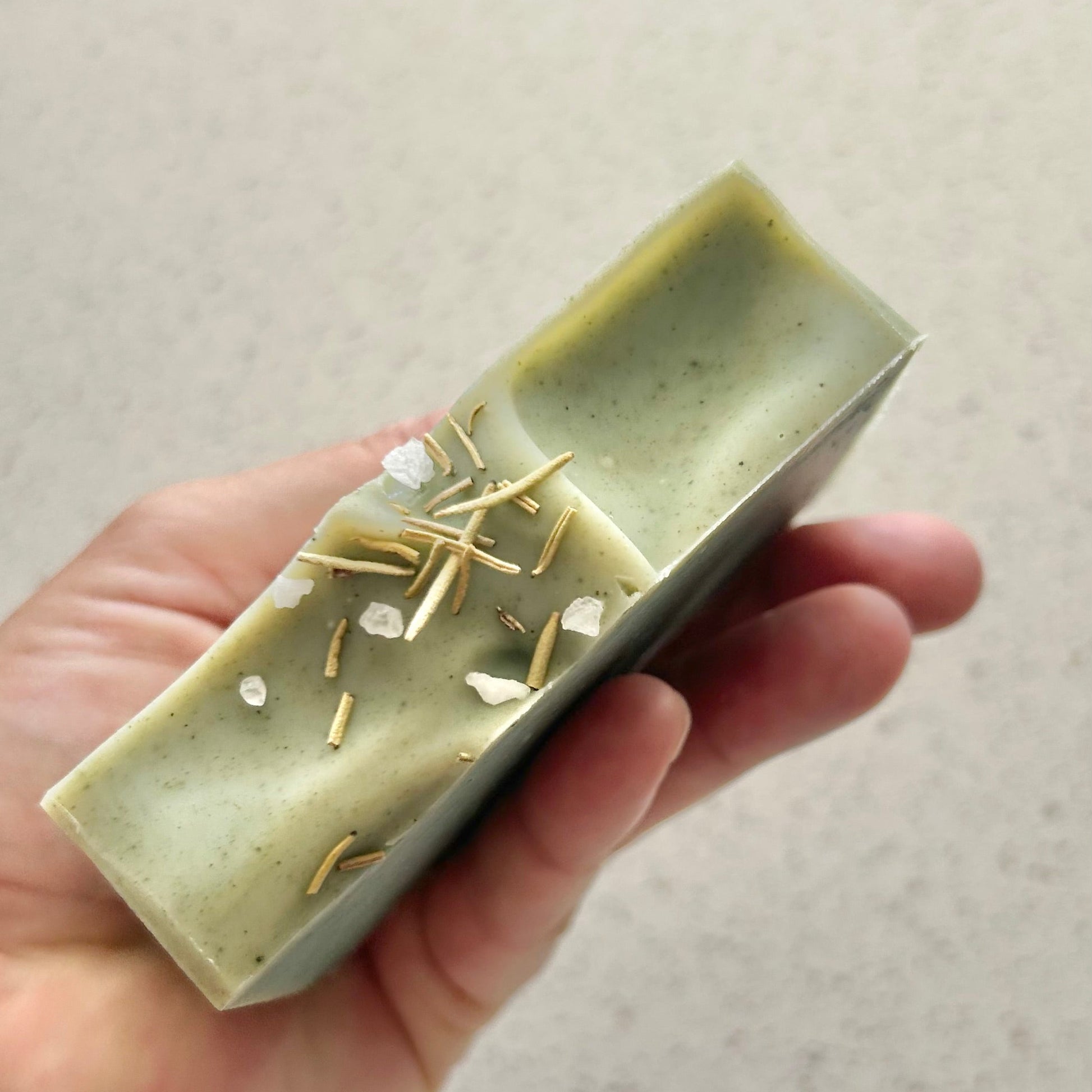 Hand holding a rectangular green soap with gold and white specks against a neutral background