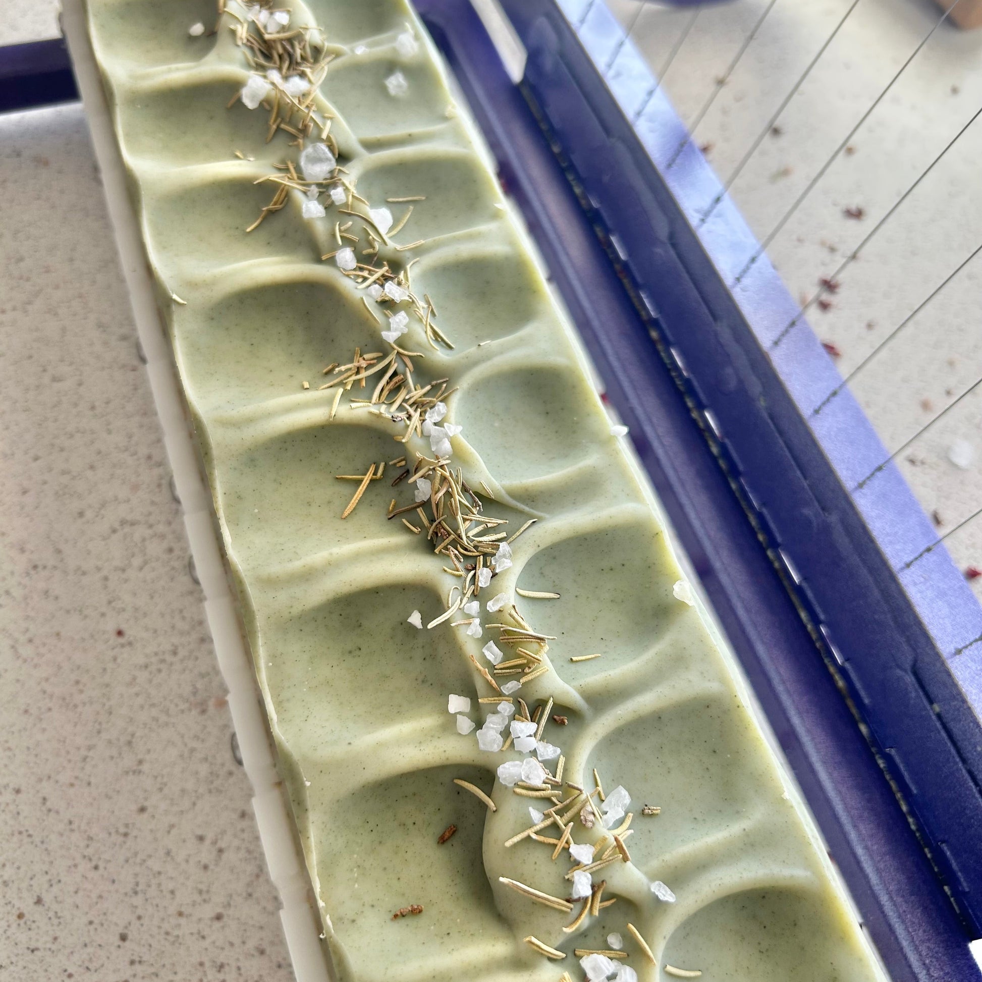Green soap bar with decorative elements in a mold on a textured surface.