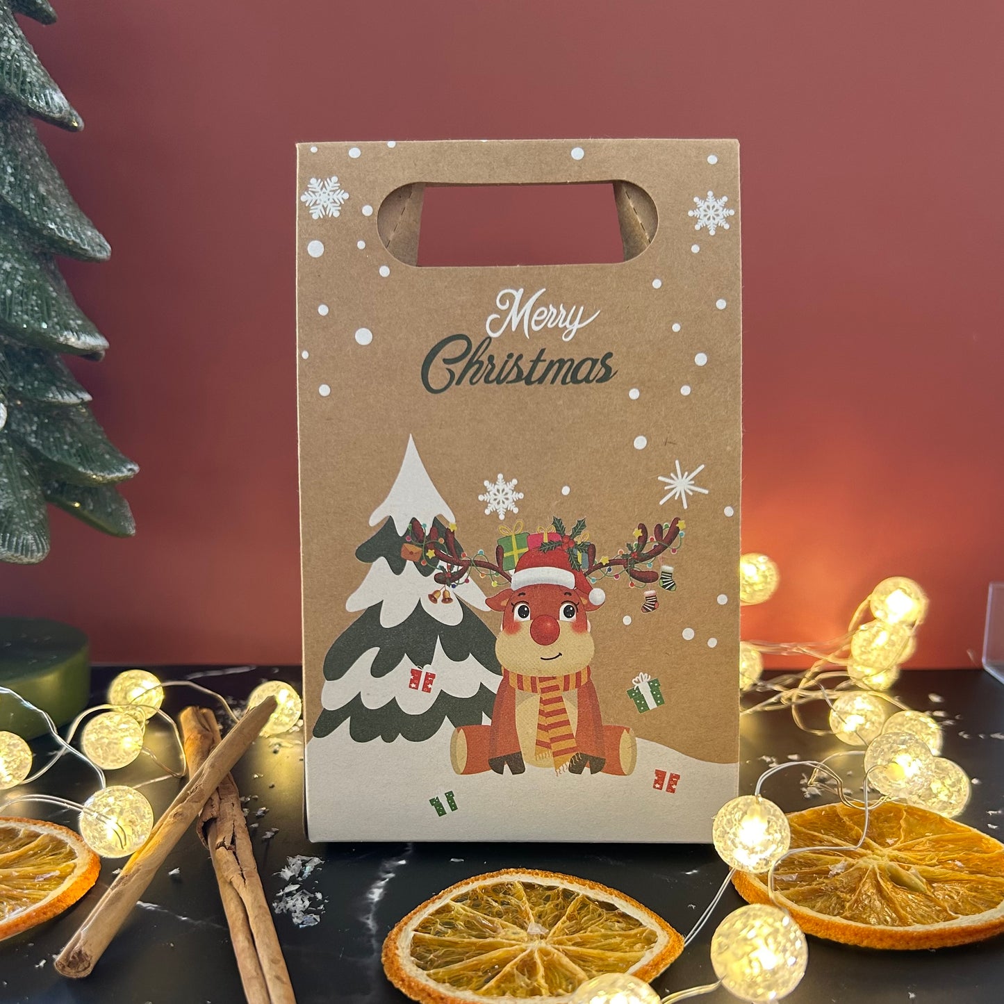 Christmas-themed gift bag with reindeer and tree design on a festive background with lights and oranges.
