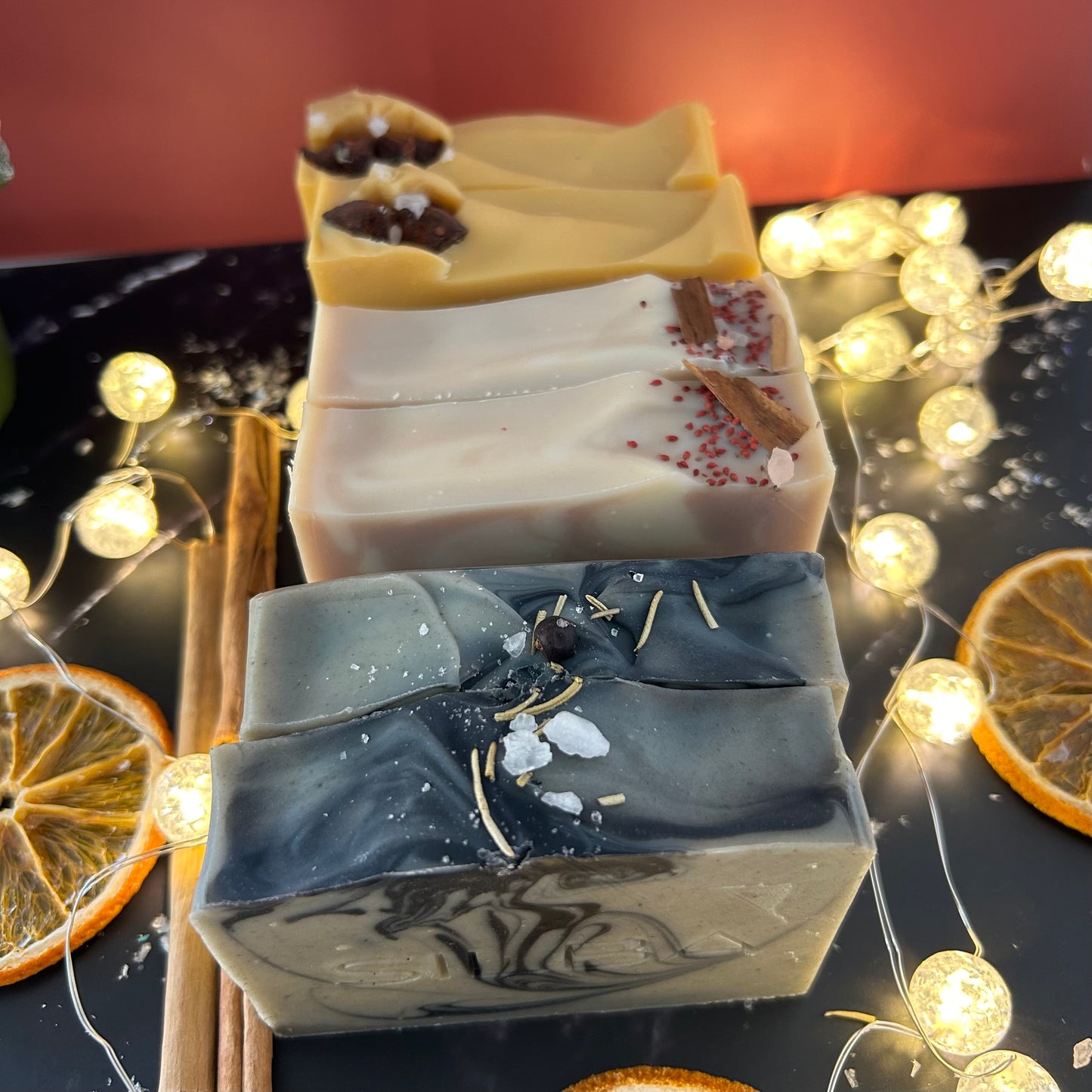 Three soap bars with decorative elements on a dark surface with string lights and orange slices.